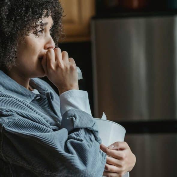 A woman holding a tissue and looking thoughtful in a kitchen.