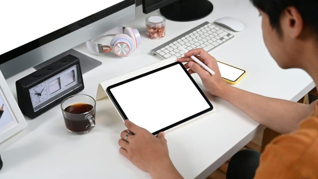 A person is using a stylus on a tablet with a blank screen, at a desk.