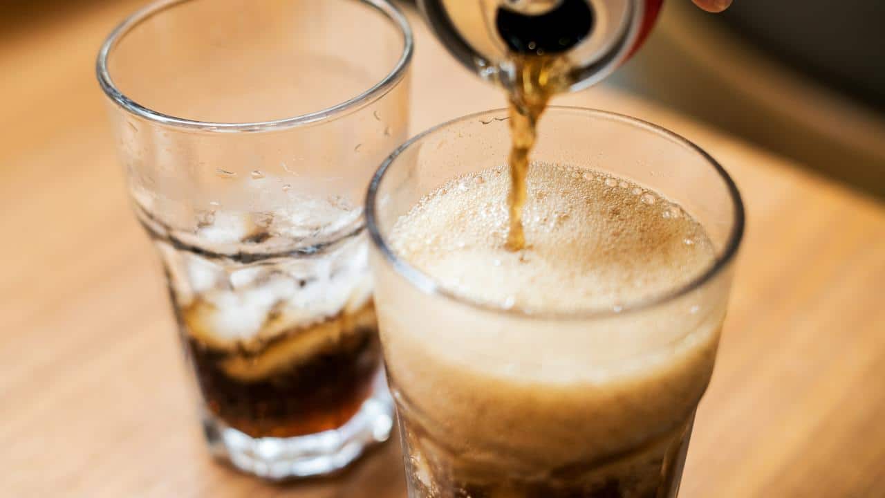 A soda being poured into a glass with ice.