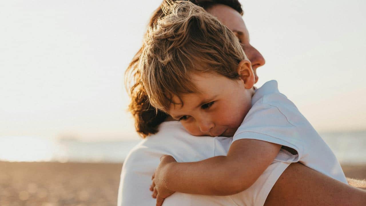 A parent hugging a sad child on the beach.