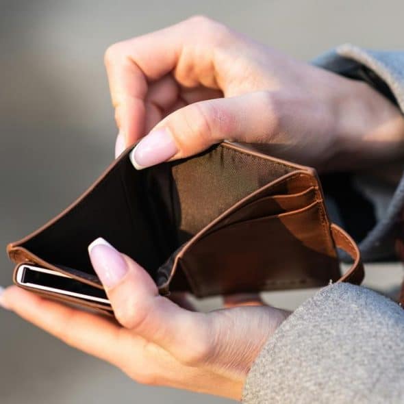 An empty brown wallet held open by a person with manicured nails.
