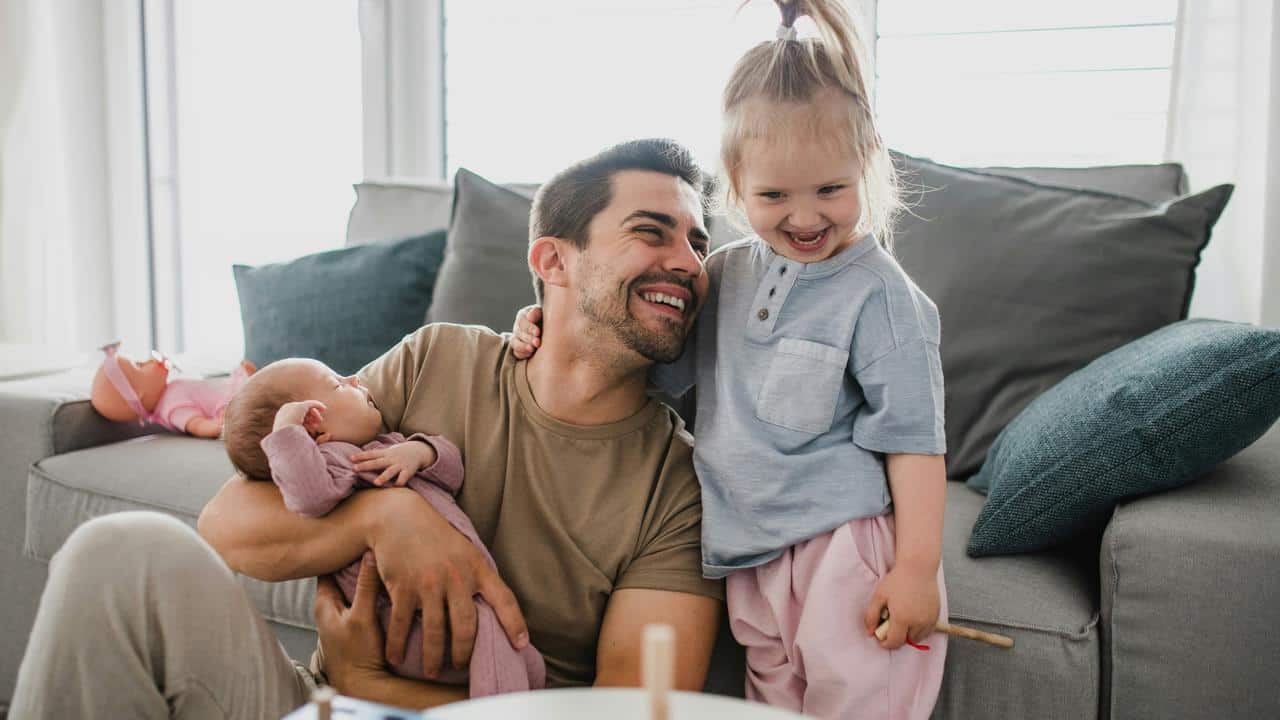 A father holding a baby and laughing with his older child.