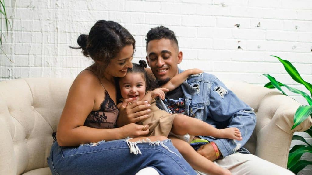 A family sitting on a couch, smiling and hugging their young child.
