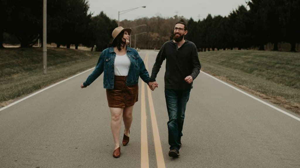 A happy couple holds hands while walking down the middle of a road.
