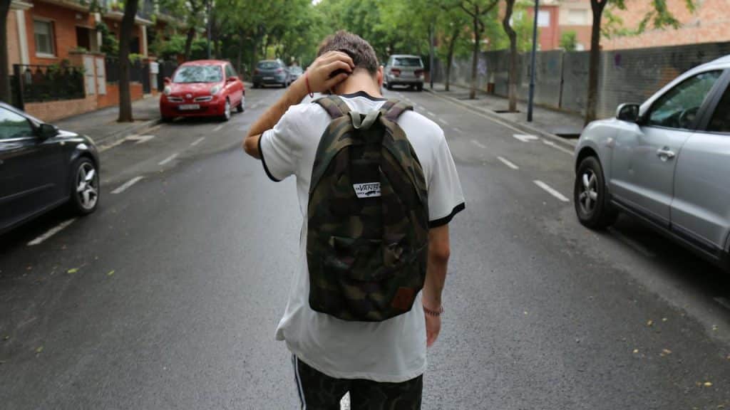A kid with a camo backpack walking alone down a street.