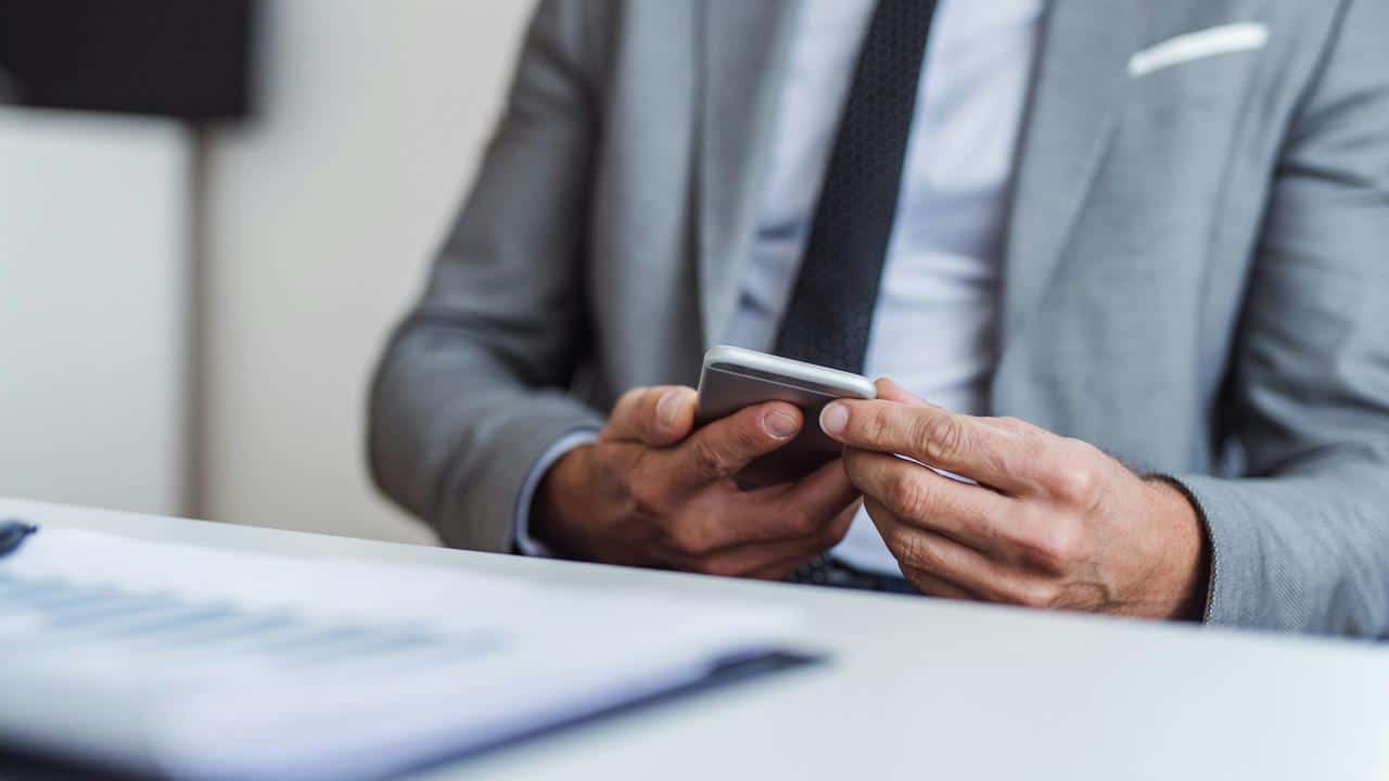 A man in a suit uses a smartphone at a desk.