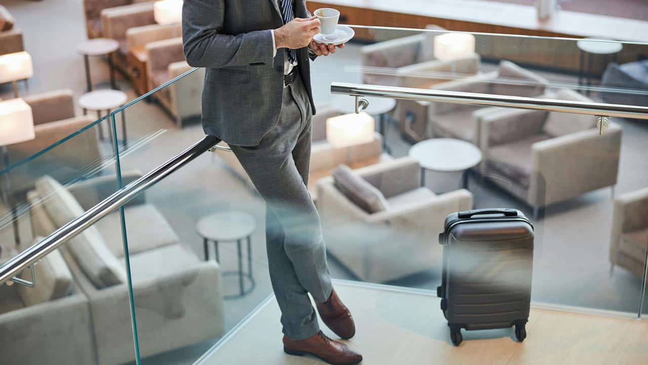A man in a suit holding coffee beside a suitcase.
