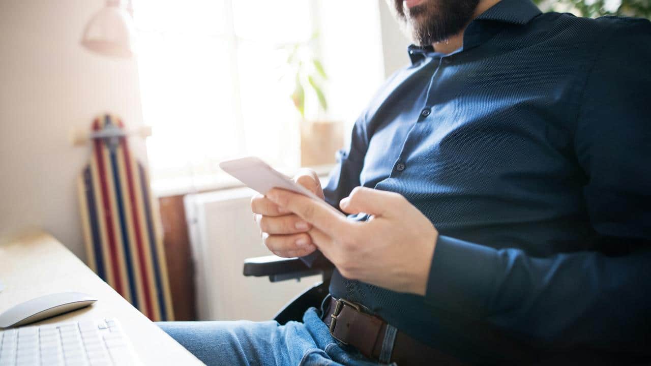A seated man in a blue shirt holding a smartphone.