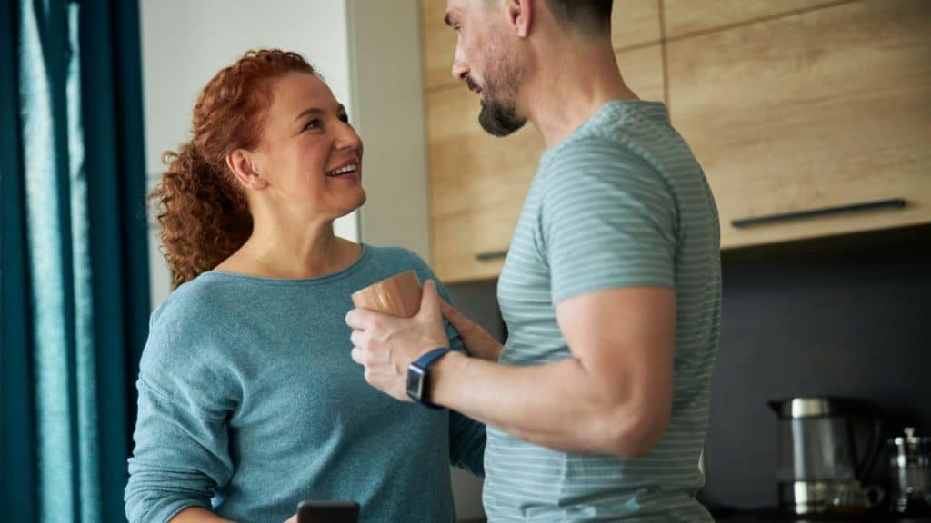 A woman with curly red hair smiles at a man holding a mug.