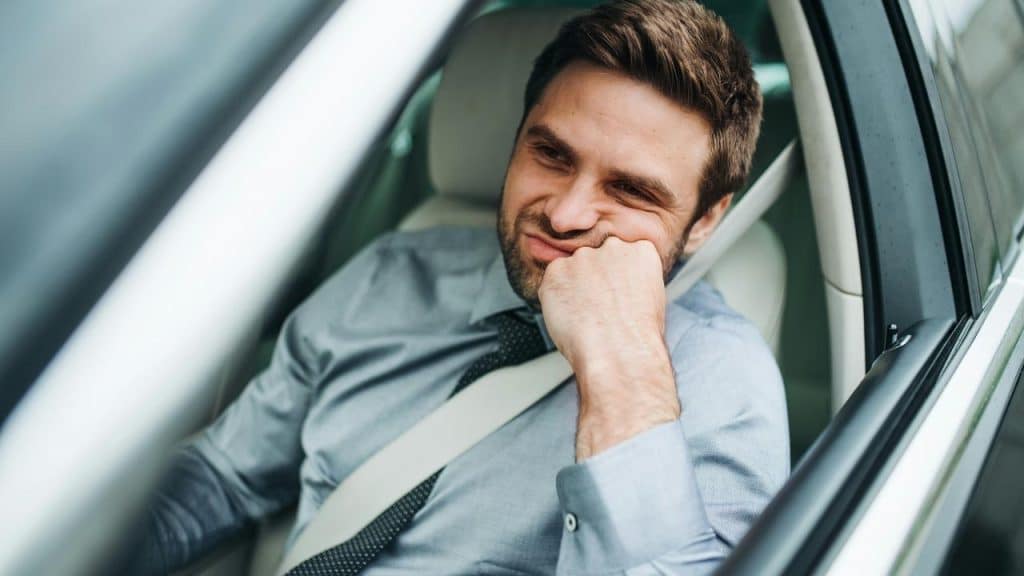 A man in a car resting his chin on his hand looking bored.