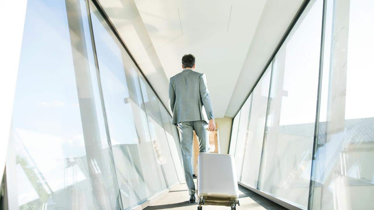 A man in a suit walking with a suitcase through a glass corridor.