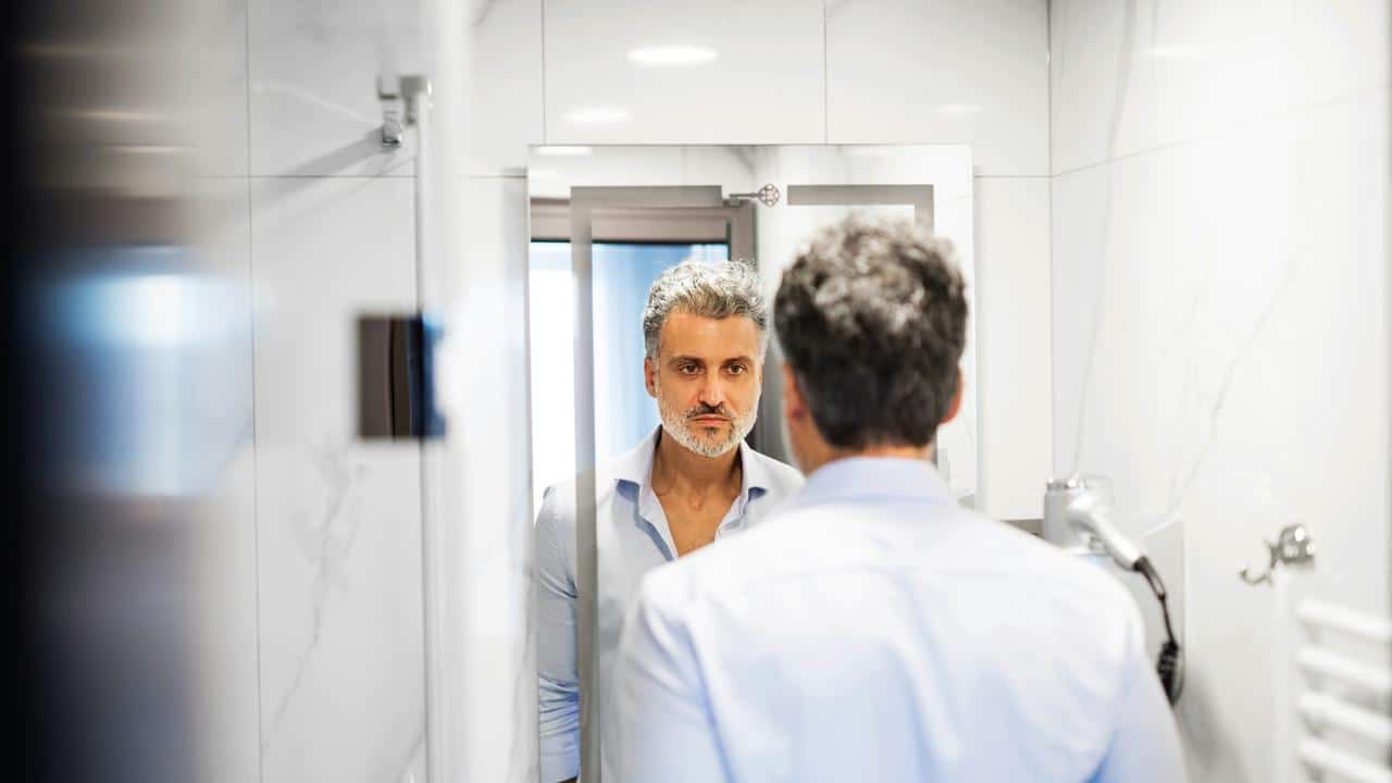 A man looking at himself in a bathroom mirror.