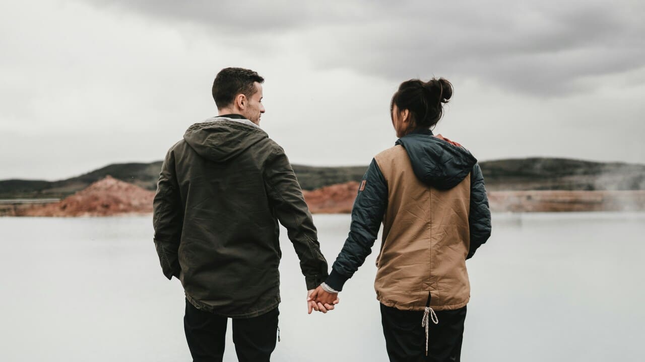 A couple holding hands while near a body of water.