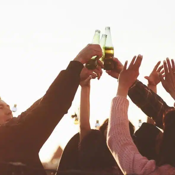 A group of friends raising beer bottles in a celebratory toast at sunset.
