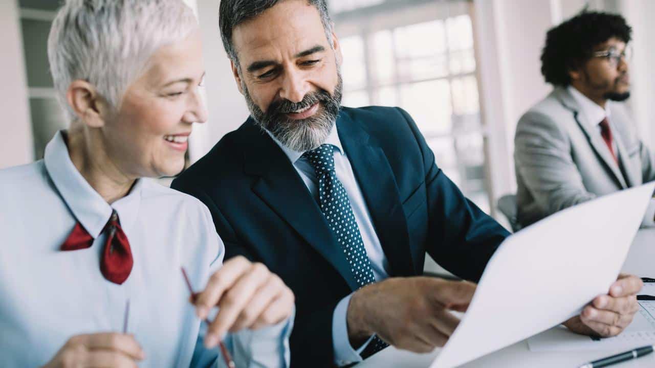 A man and a woman in business attire reviewing a document together.