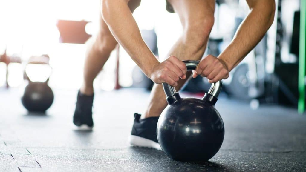 A man gripping a kettlebell during a strength training workout at the gym.