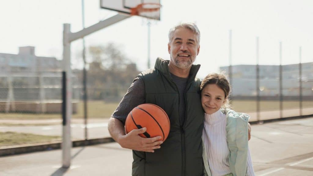 A man holding a basketball while standing next to a smiling girl on an outdoor court.