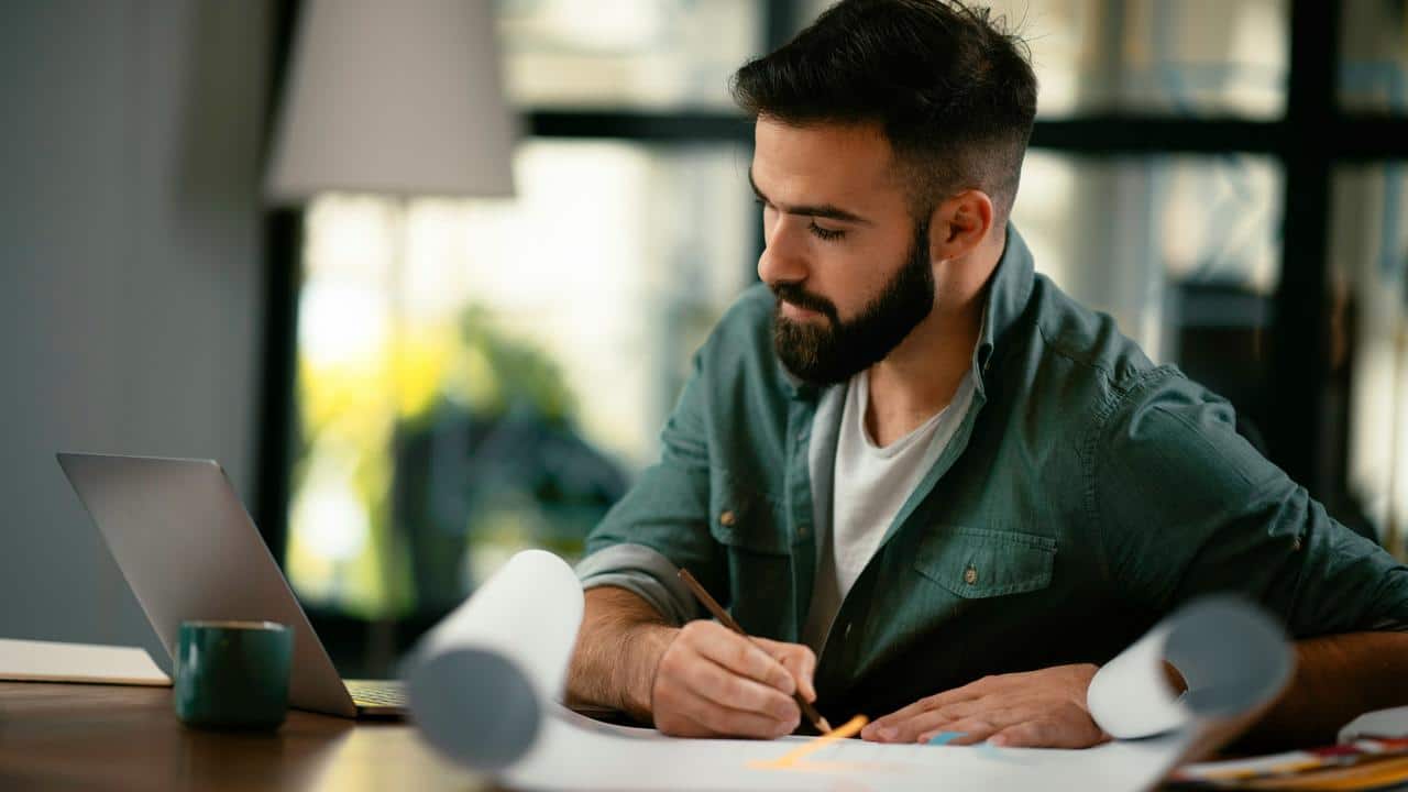 A man sketching at a desk with a laptop.