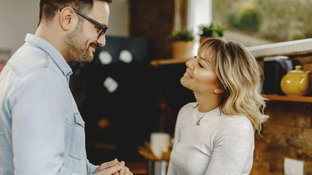 A man in glasses and a woman with wavy hair smile at each other.