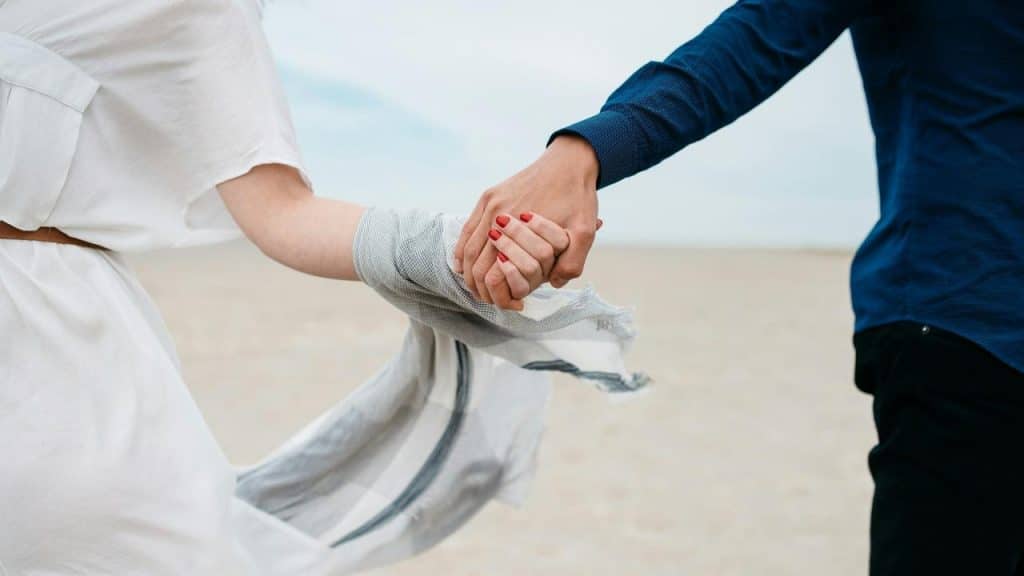 A couple holding hands while walking on a beach.