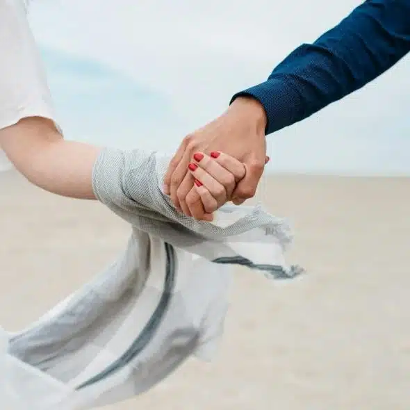 A couple holding hands while walking on a beach.