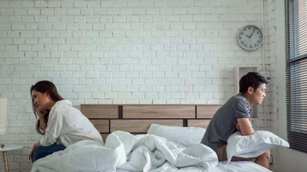Man sitting on the edge of the bed while wife is planning to leave the room