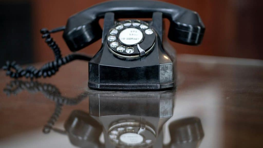 A vintage black rotary telephone on a reflective surface.