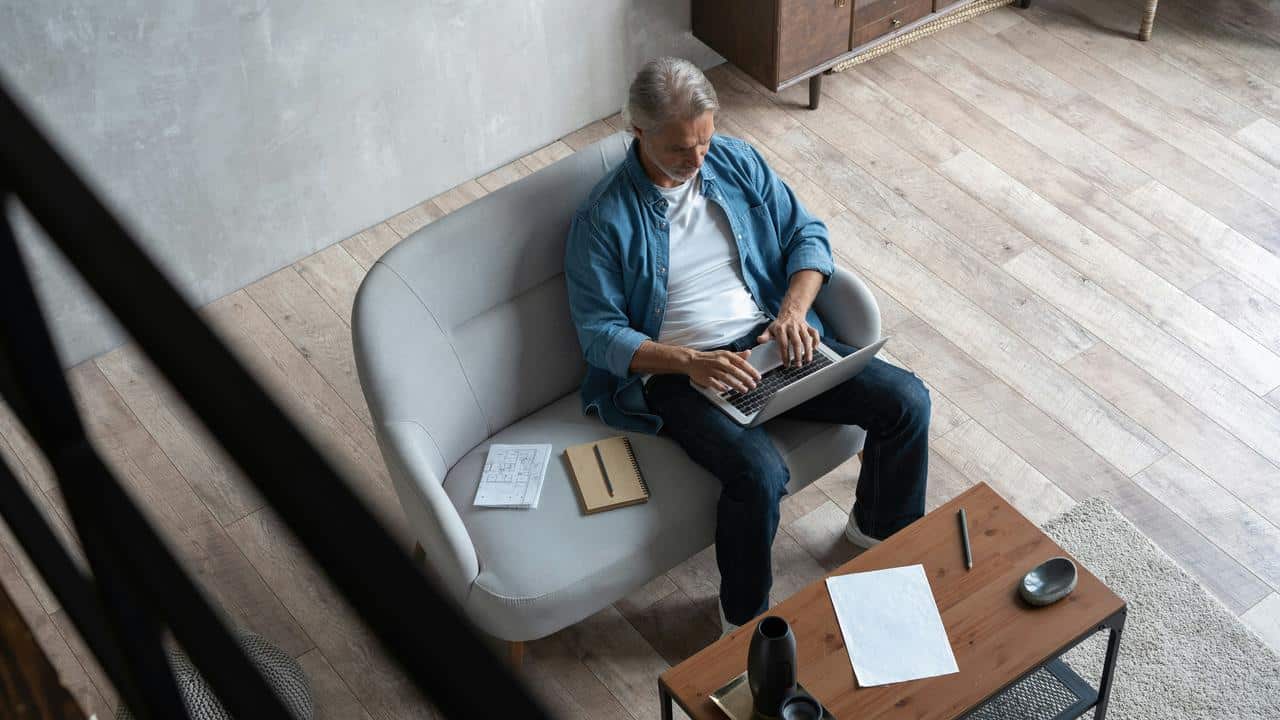 A man seated on a sofa working on a laptop.