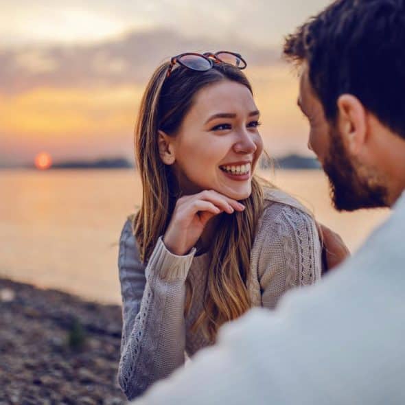 A couple smiling and talking by a lakeside at sunset.