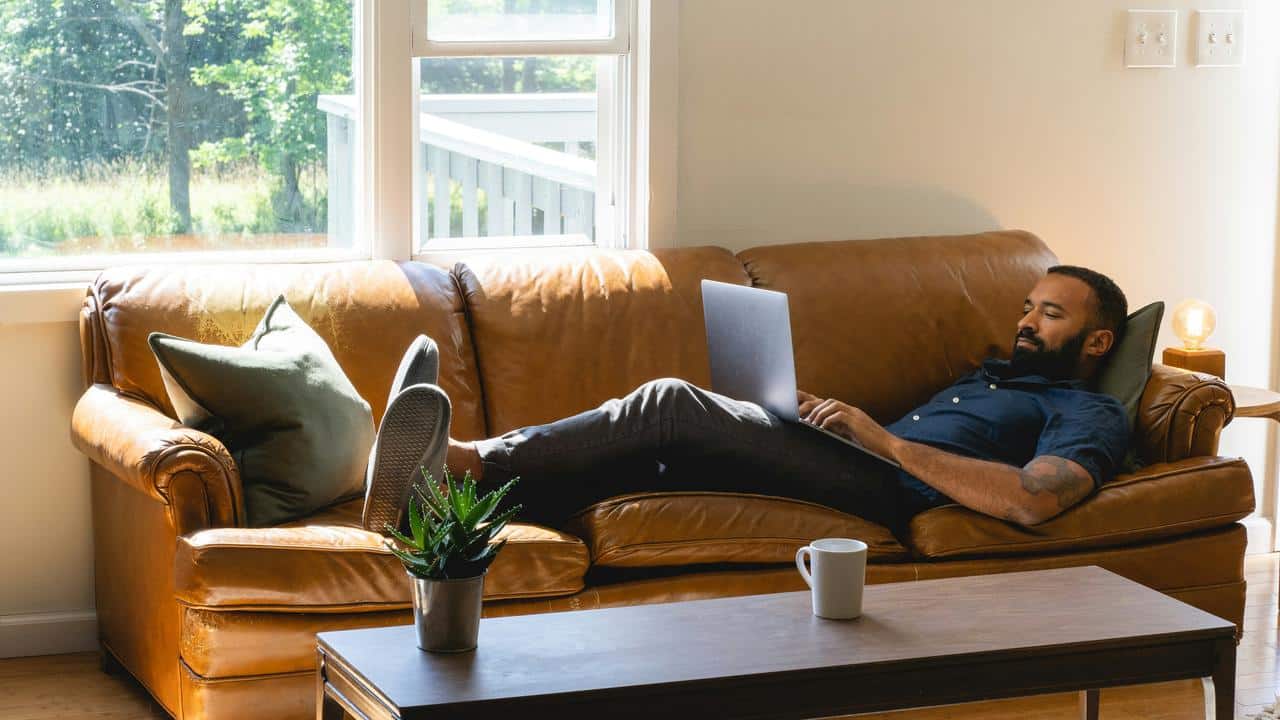 A man working on a laptop while lying on a couch.
