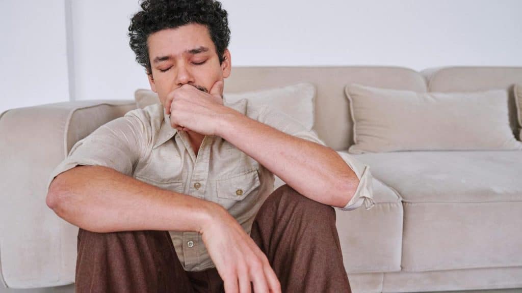 A man sitting on the floor with eyes closed and hand over his mouth.