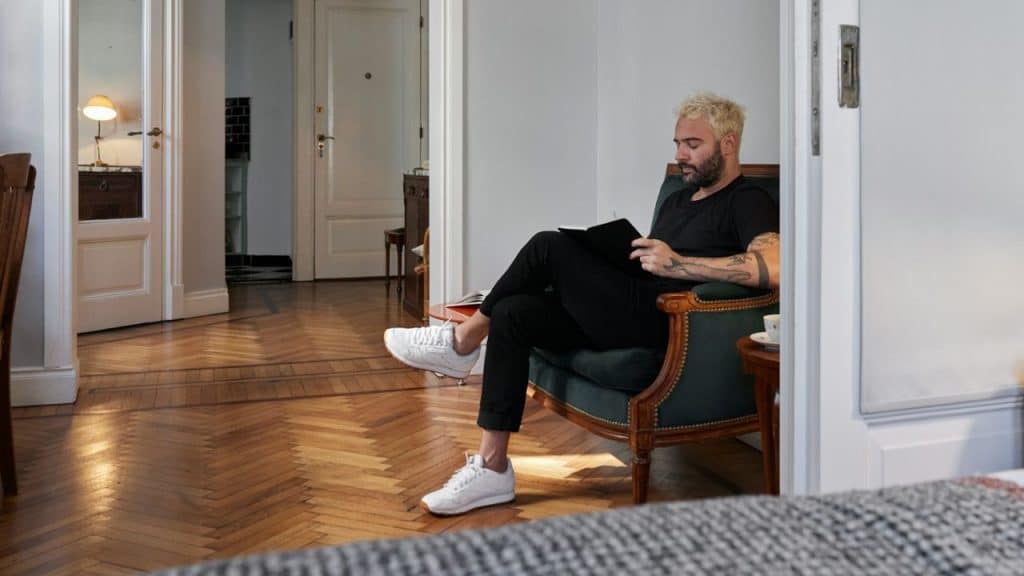 A platinum-blonde man in a black shirt reads a book in an armchair.