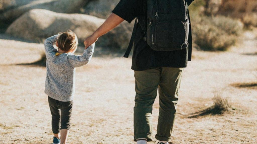 A man and a kid holding hands while walking outdoors.
