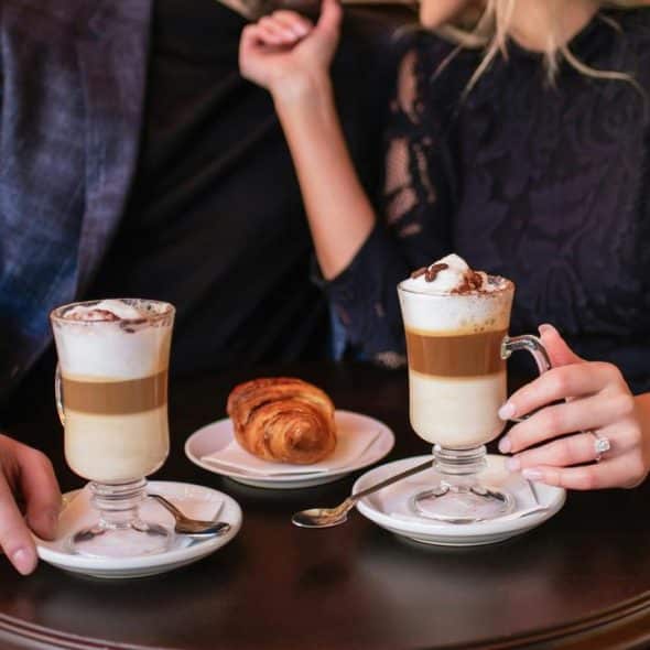 A couple enjoying lattes and a croissant at a café table.