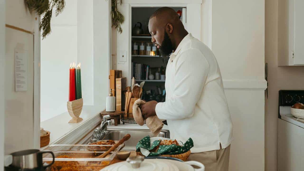 A man in a kitchen drying dishes near a counter with food and candles.