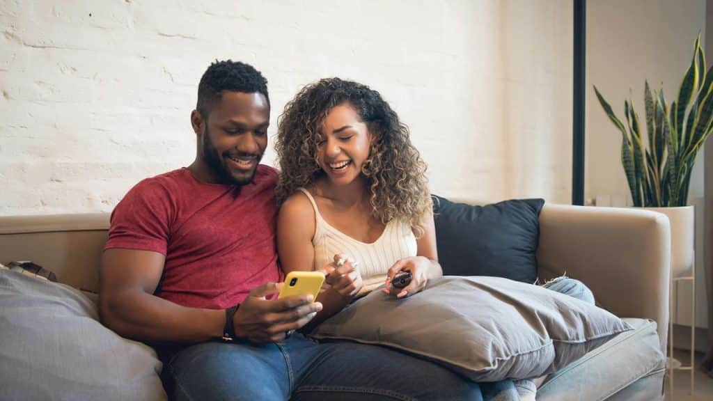 A couple laughing while looking at a phone on a couch.