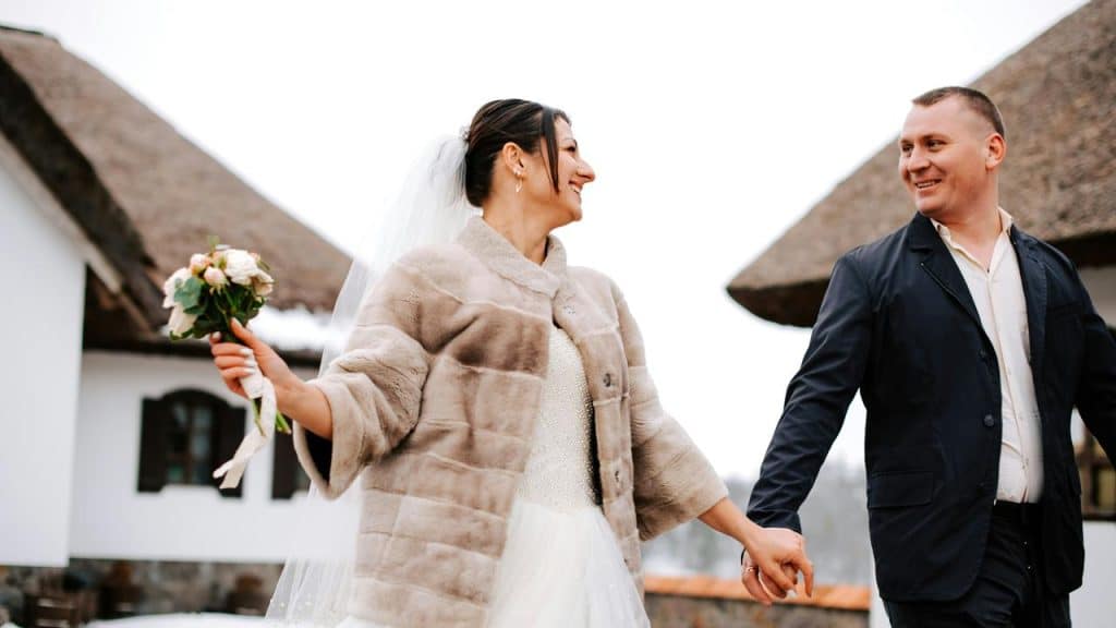 A bride and groom holding hands and smiling outdoors.
