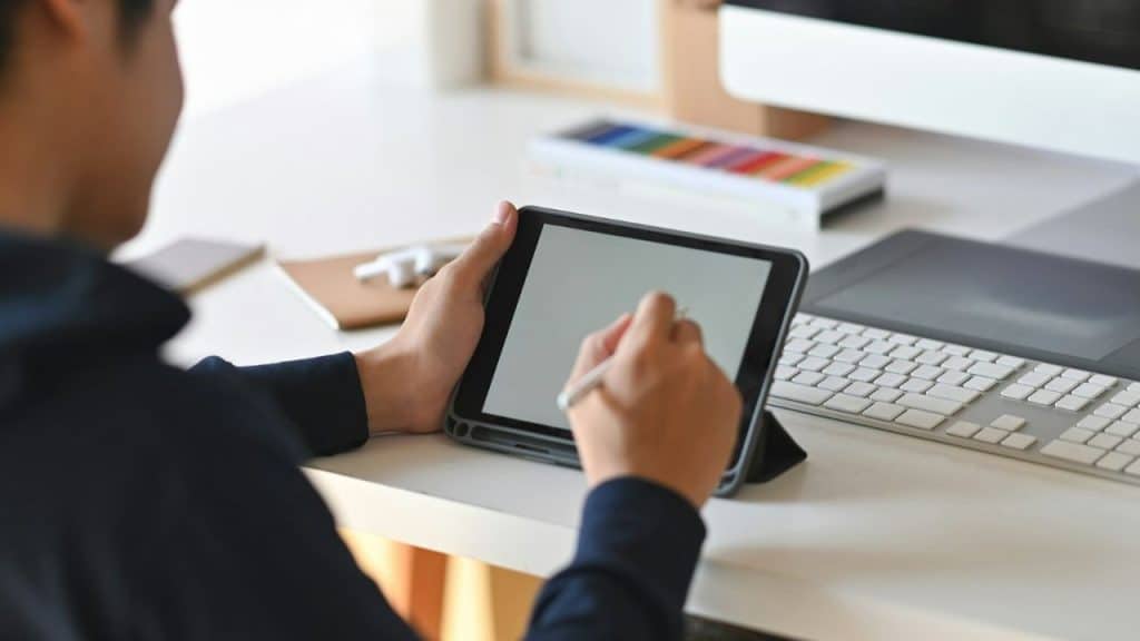 A person from behind is drawing on a tablet with a stylus at a desk.