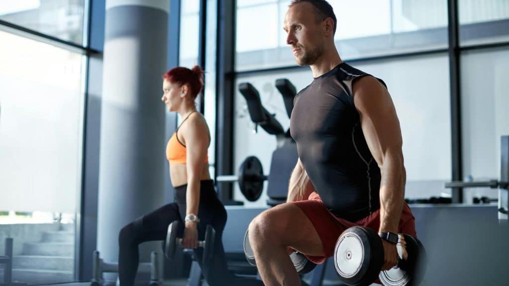 A couple doing dumbbell lunges at the gym.