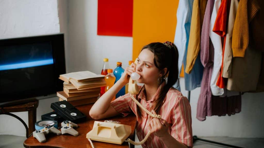 A woman on a vintage rotary phone at a cluttered desk.