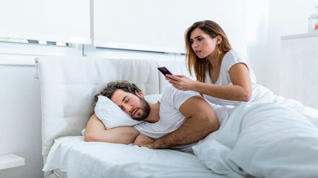 A woman looking at her man’s phone while he sleeps