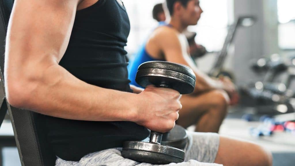 A man holding a dumbbell while seated at the gym.