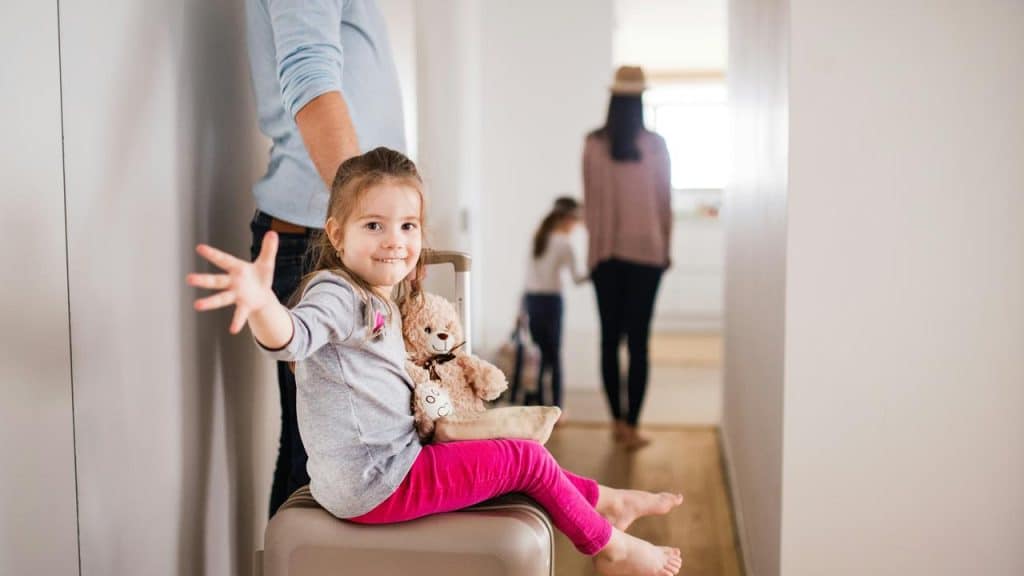 A kid smiling while sitting on a suitcase with a teddy bear.