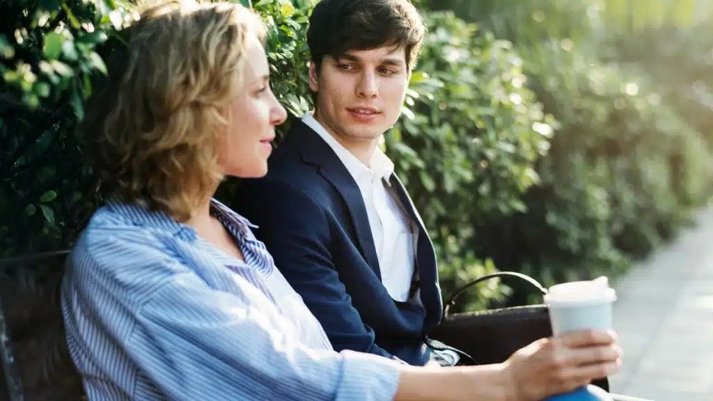 A couple talking on a bench with a coffee cup in hand.