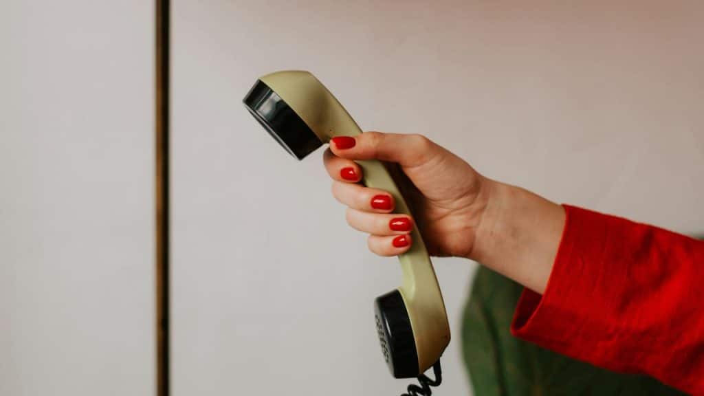 A hand with red nails holding a vintage telephone receiver.