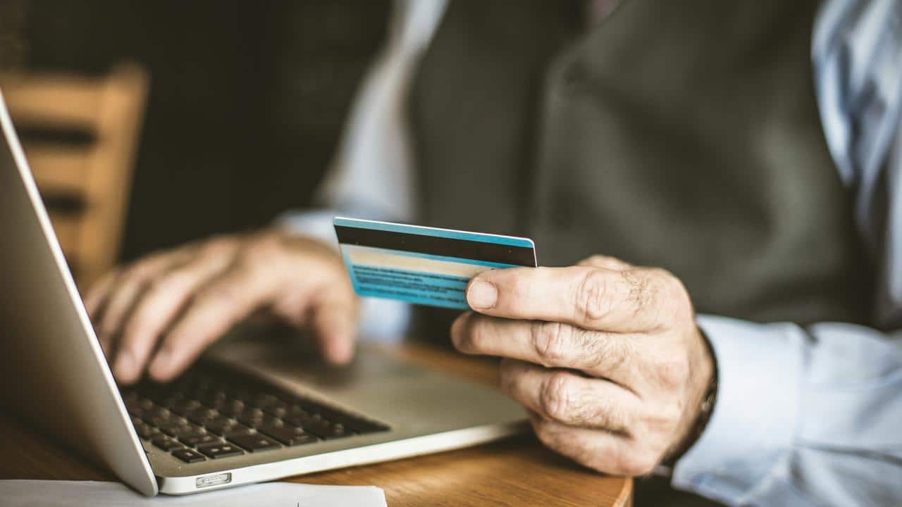 A man holds a credit card while using a laptop.