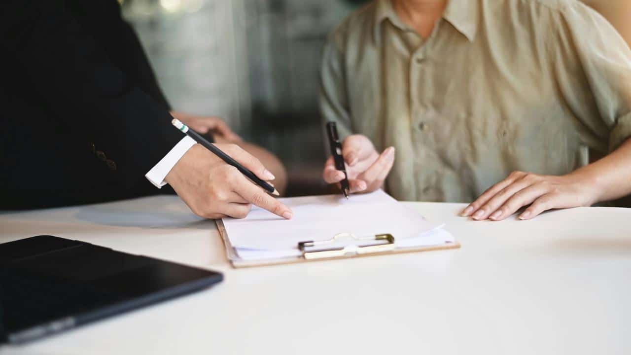 A person signing a document on a clipboard.