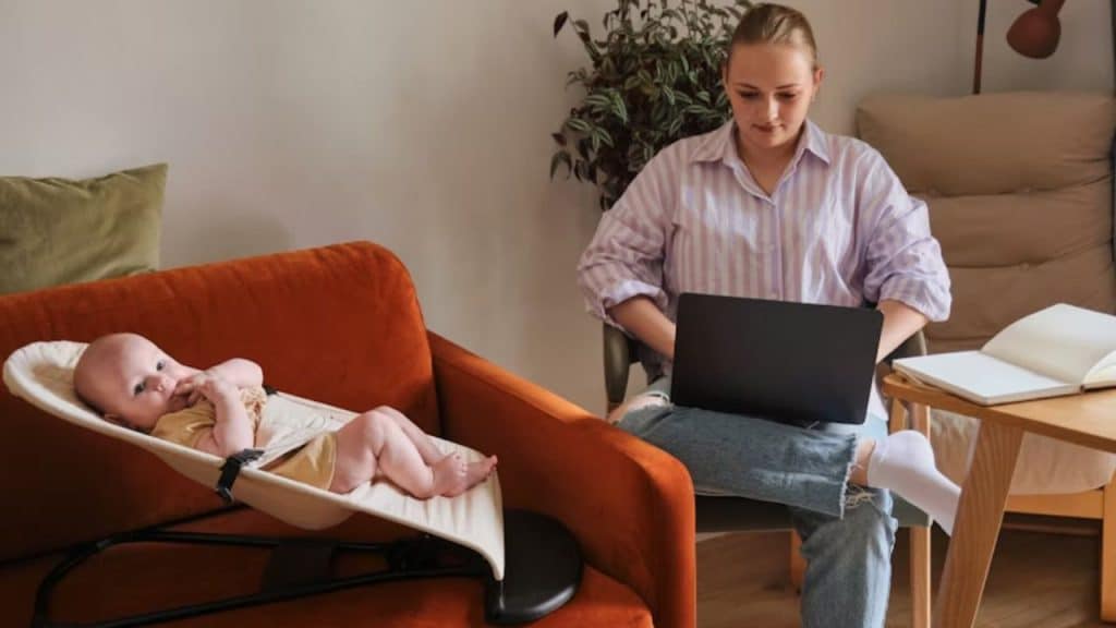 A woman multitasking with laptop while watching over the baby