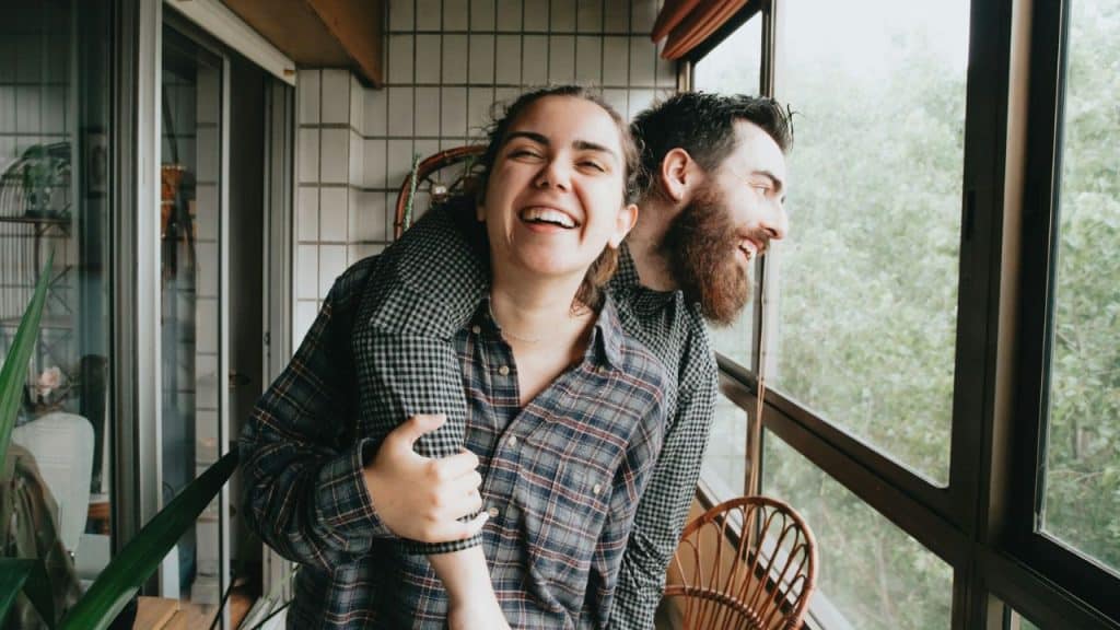 A laughing woman embraces a smiling man on a balcony.