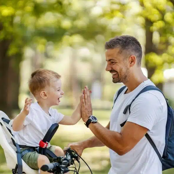 A man and a kid sharing a high five during a bike ride in a sunny park.